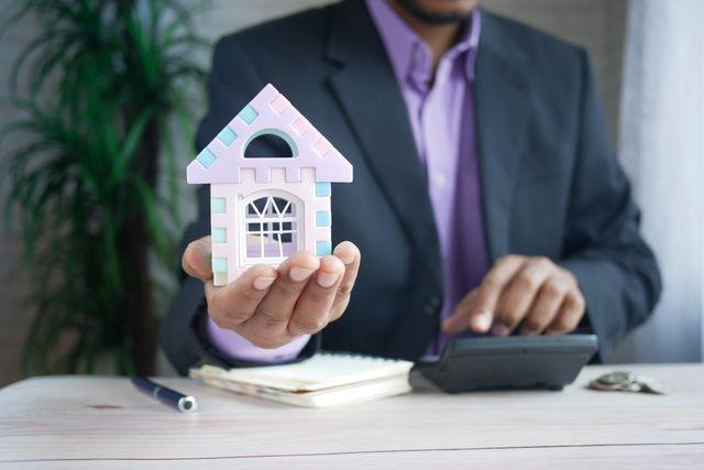 a person using a calculator and holding a small house model
